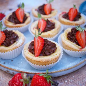 Diese veganen Käsekuchen-Cupcakes sind einfacher gemacht, als gedacht und total lecker mit cremiger Käsekuchenfüllung, fruchtigen Erdbeeren und Schokolade on Top!